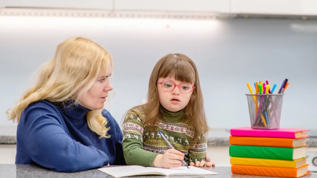 A girl with Downs Syndrome works with a teacher at school. 